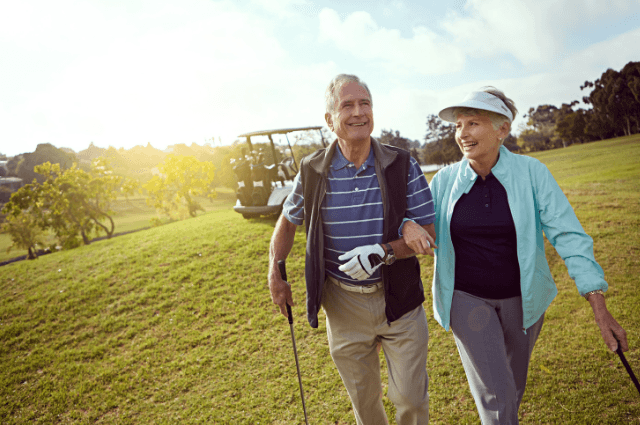 Couple walking on a golf course with a golf club and linking arms.
