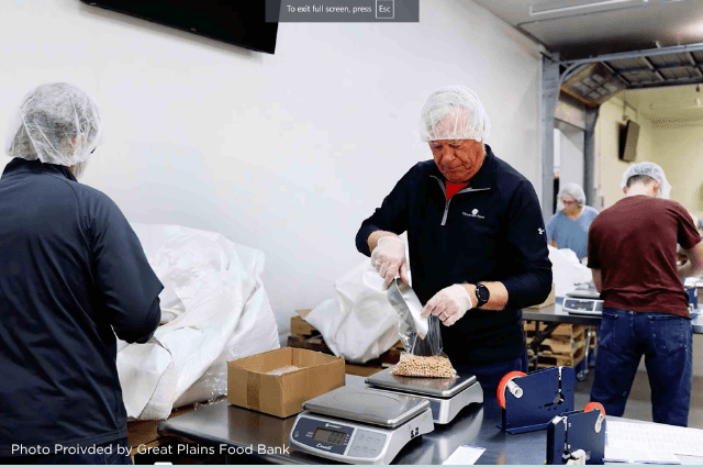 People wearing gloves and hair nets packing food in a warehouse.