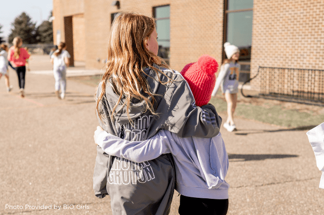 Two girls hugging and walking in a parking lot.