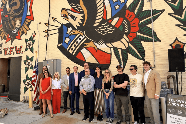 Group of people standing in front of a brick wall with a mural of an eagle and bison.