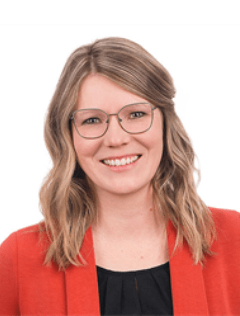 Woman wearing glasses with a red blazer in front of a white background.