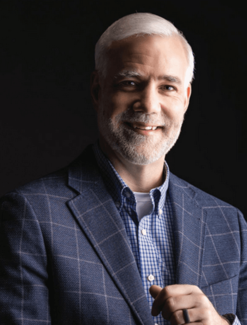 Man in front of a black background wearing a suit coat.
