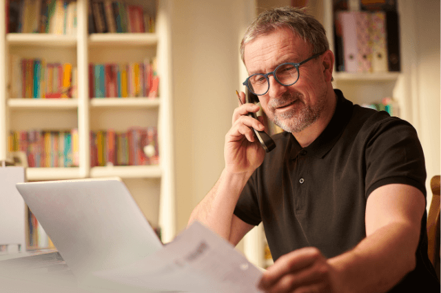 Man with glasses talking on the phone and looking at papers.