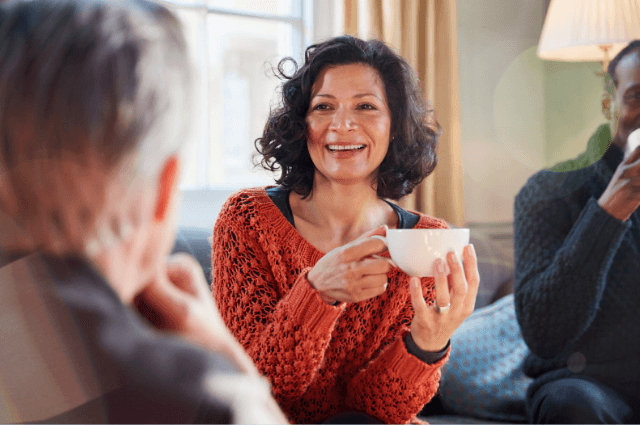 Woman sitting on a couch smiling holding a coffee cup.