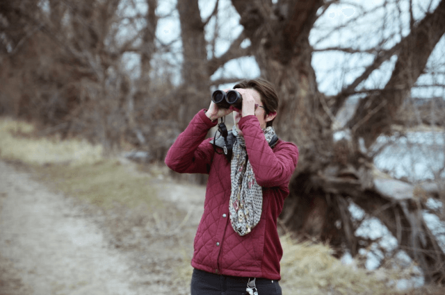 A person standing outside by trees using a pair of binoculars.