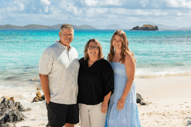 Family standing on a beach smiling.