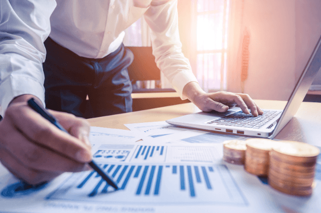 Papers on a desk with a person holding a pen and pointing at a chart.