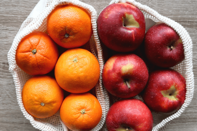 A bag of oranges and a bag of apples next to each other.